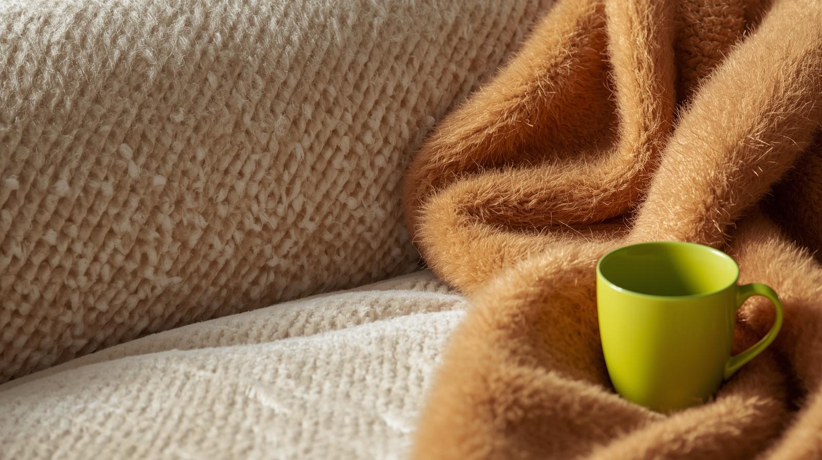 Ein grüner Becher auf einer flauschigen orangefarbenen Decke über einer cremefarbenen strukturierten Couch.